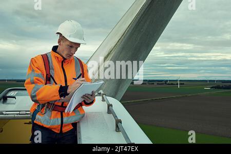 Making sure he has everything on his checklist. a young engineer inspecting a wind turbine. Stock Photo