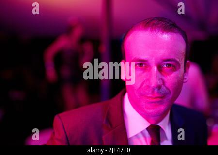 Unwinding in the wrong kinda way. a seedy businessman in a neon lit go go bar with a woman dancing on a pole behind him. Stock Photo