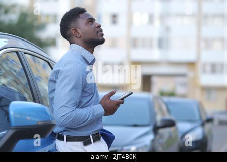 Handsome young businessman using smartphone while standing near his car outdoors, copyspace Stock Photo