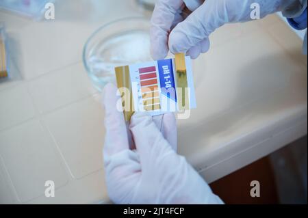 Close-up lab technician's hands in medical gloves, holding a litmus or reagent paper, conducting PH test in medical lab Stock Photo