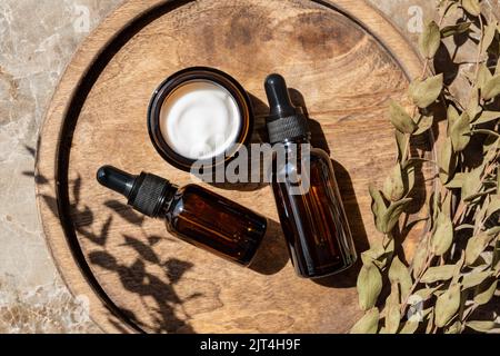 Amber glass bottles and jars with natural cosmetics and eucalyptus on wooden tray on table in bathroom. SPA organic bio cosmetics set. Stock Photo