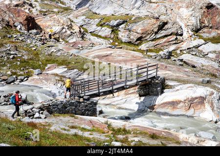 Hikers crossing old wooden bridge over glacier creek on a beautiful Innergschlöss Glacier Trail to Schlatenkees glacier, East Tyrol, Austria Stock Photo