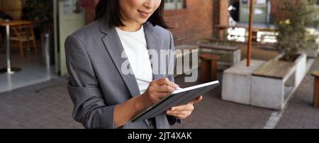 Happy professional woman taking notes using digital tablet standing outside. Stock Photo