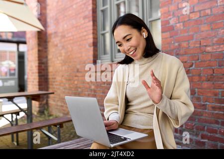 Young Asian woman using laptop video calling having virtual meeting outdoor. Stock Photo