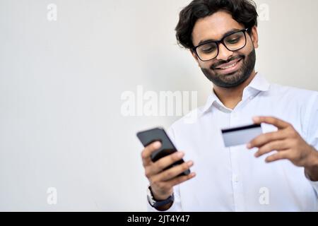 Smiling young indian business man using phone holding credit card. Stock Photo
