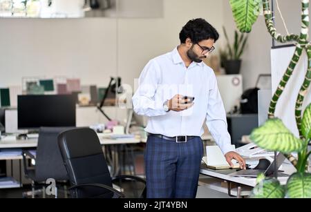 Busy young indian male manager working standing in office at workplace. Stock Photo
