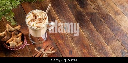 Glass of traditional Christmas drink eggnog with whipped cream and cinnamon, Xmas cookies stars on rustic wooden background. Cozy Xmas time concept. B Stock Photo
