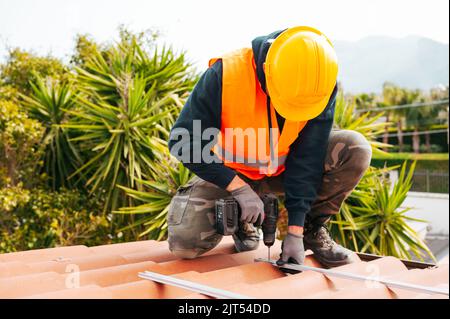 Technical worker works with drill on the roof of a house Stock Photo