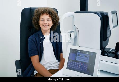 Smiling curly-haired boy in ophthalmologist office during consultation and eye examination on modern ophthalmological equipment Stock Photo