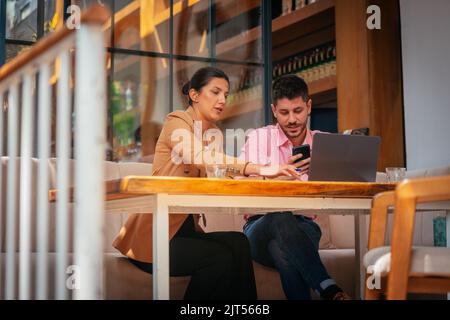 Two young businesspeople having conversation in cafe bar on a summer day, view from side, wide shot, low angle Stock Photo