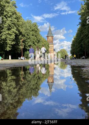 Kaliningrad, Russia. 15th July, 2022. People walk in a city park past a puddle in which part of a church is reflected. Credit: Ulf Mauder/dpa/Alamy Live News Stock Photo