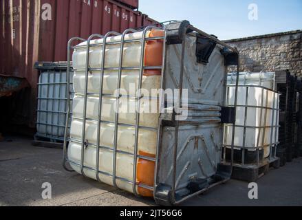 Heavily used old white intermediate bulk container or IBC plastic tank with twisted metal cage put on top of wooden pallets at local construction site Stock Photo