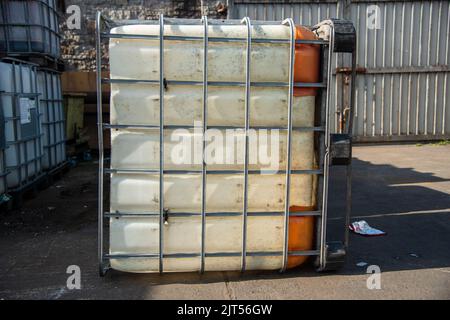 Heavily used old white intermediate bulk container or IBC plastic tank with twisted metal cage put on top of wooden pallets at local construction site Stock Photo