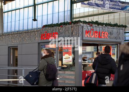 Stuttgart, Germany - December 31, 2021: Shopping in butcher shop. Snack bar in main station hall is decorated for Christmas. Stock Photo