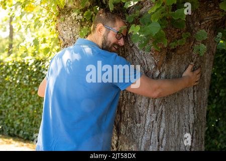 Happy young caucasian man looking away while embracing tree trunk at park Stock Photo