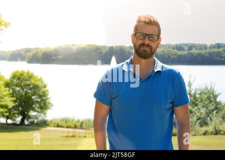 Handsome young man in polo t-shirt standing in a park. Stock Photo