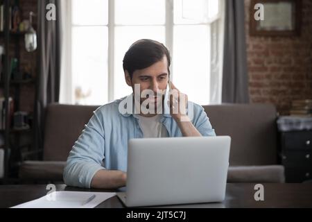 Serious freelance business man talking on mobile phone at laptop Stock Photo