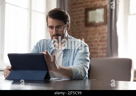 Focused millennial freelance employee man in casual using tablet computer Stock Photo