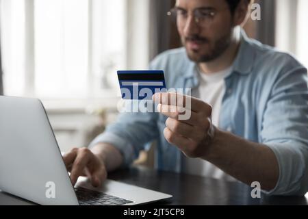 Millennial man using computer, holding credit card at camera Stock Photo