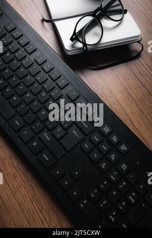 Background image of wood vintage desk focused on keyboard with notepad and glasses. Workplace. Stock Photo