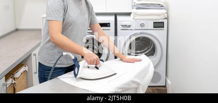 ironing white shirt on board in laundry room with washing machine on background Stock Photo