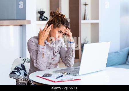 Young frustrated woman working at office desk in front of laptop suffering from chronic daily headaches, treatment online, appointing to a medical con Stock Photo