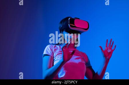 Young woman wearing VR headset while working with engineering project in lab with three dimensional printing in neon light studio. High tech Stock Photo