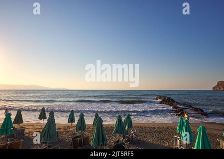 Empty sunbeds and umbrellas on the beach at sunset time in Chania Crete - Greece Stock Photo