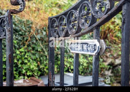 An old rusted iron gate with a notice reading please shut the gate, has been left ajar Stock Photo