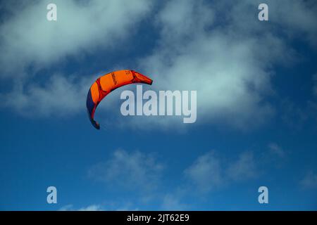 An orange para sail set against a clouded blue sky Stock Photo