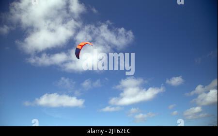 An orange para sail set against a clouded blue sky Stock Photo