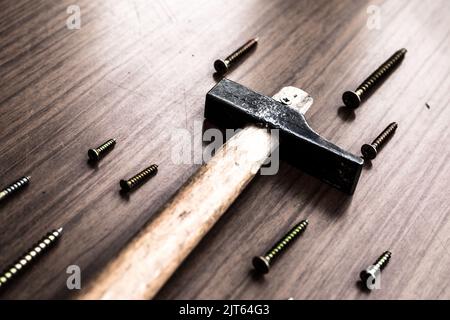 A sledge hammer and screws next to it on wooden background. Stock Photo