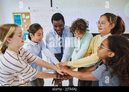 High angle portrait of diverse schoolchildren huddling in team exercise in classroom and stacking hands Stock Photo