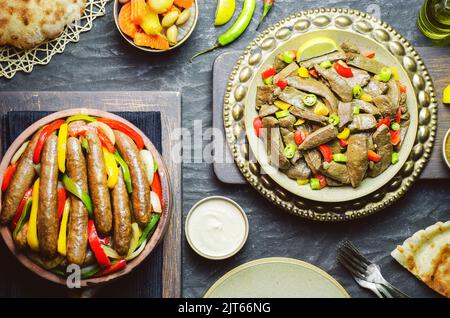Arabic cuisine; Egyptian Traditional sausage and liver dishes. Served with fresh pita bread, pickles, tahini sauce and lemon. Top view with close up. Stock Photo