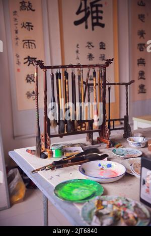Paint brushes of a traditional chinese painter artist hanging on the table together with the oil paints Stock Photo