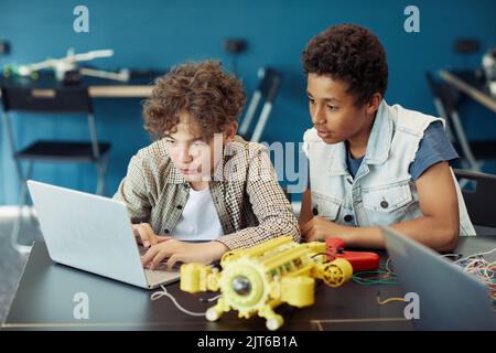 Portrait of two teenage boys using laptop and programming robot during engineering class in school Stock Photo