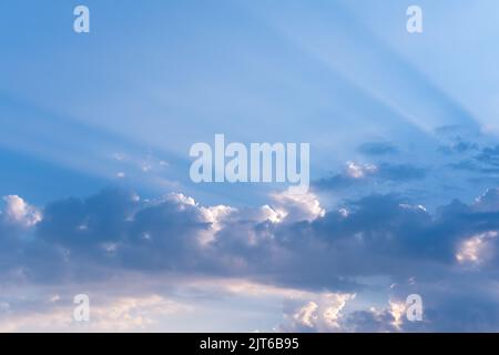 Evening sky with illuminated clouds, amazing sunset and majestic sunlight breaking through the clouds and leaving streaks of rays on the background of Stock Photo
