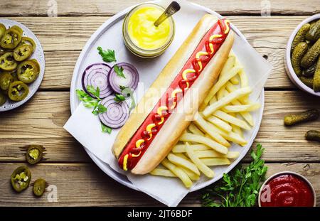 Hot dog served with French fries, Gherkin pickles, jalapeno slices, fresh onion, fresh parsley, honey mustard and ketchup. Top view with close up. Stock Photo