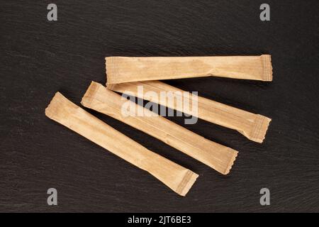 Four sticks of sugar in paper bags on a slate stone, close-up, top view. Stock Photo