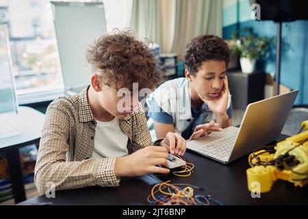 Portrait of two boys using laptop together and programming robots during engineering class at school Stock Photo