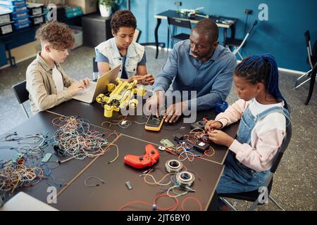 High angle view at diverse group of kids building robots during engineering class at school with male teacher helping Stock Photo