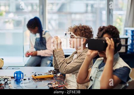 Side view portrait of two kids building robots in engineering class and using VR technology Stock Photo