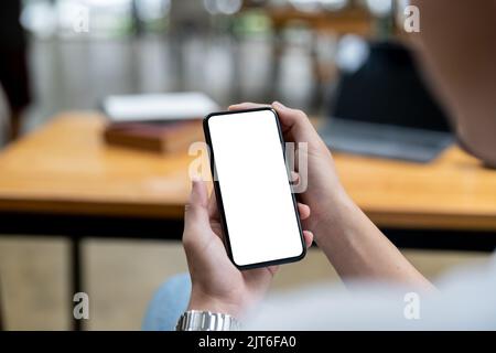 Mockup image of a woman holding black mobile phone with blank white screen while sitting in cafe. Stock Photo