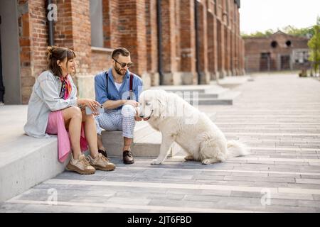 Stylish couple have fun and sit with their dog on a street Stock Photo