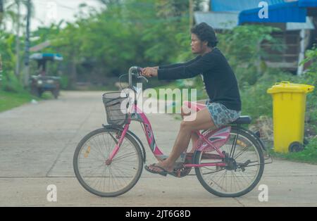 A funny moment as a man rides a bicycle, sitting on the carrier. Stock Photo