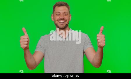 Like. Bearded handsome young man raises thumbs up agrees with something or gives positive reply recommends advertisement likes good. Adult guy isolated alone on chroma key studio background indoors Stock Photo