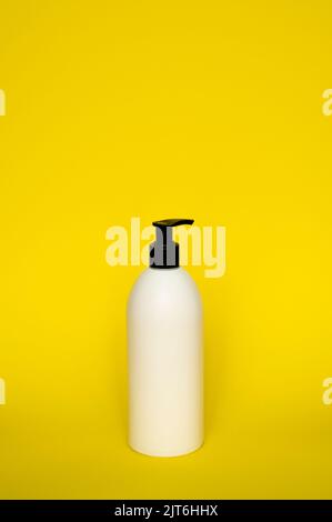 White cosmetic plastic bottle with black pump dispenser on yellow background. Liquid container for gel, lotion, cream, shampoo, bath foam. Stock Photo