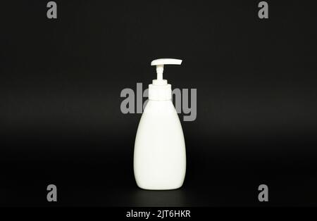 White plastic bottle with black dispenser, isolated on black background. Stock Photo