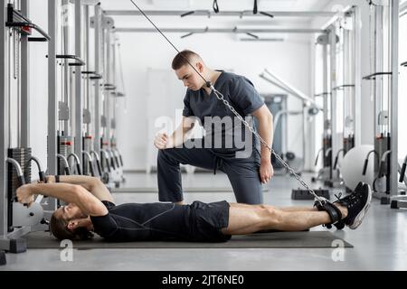Man doing exercises on decompression simulators with the help of rehabilitation specialist Stock Photo