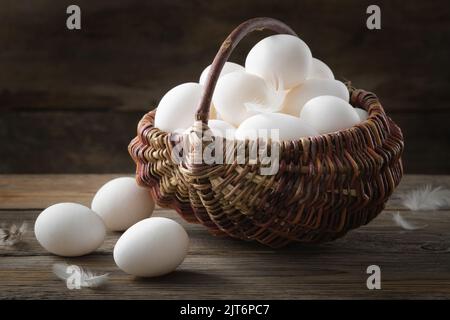 Wicker basket full of white chicken eggs on wooden table. Stock Photo